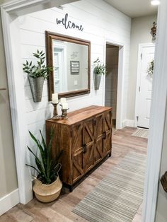 a room with a mirror, potted plants and a wooden cabinet on the floor