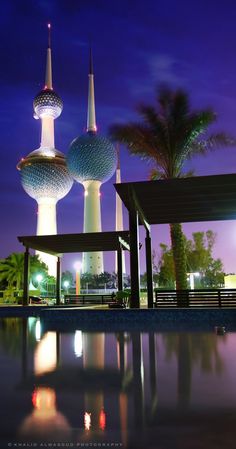 some very tall buildings with towers in the background at night or dawn, near a pool