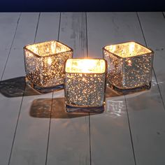 three glass candle holders sitting on top of a wooden floor next to eachother