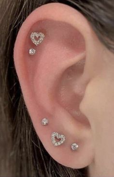 a woman's ear with three heart shaped diamond studs on the middle of it