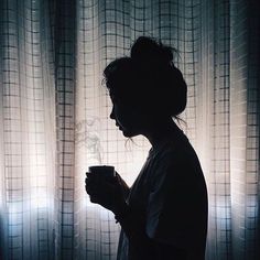 a woman standing in front of a window holding a cup