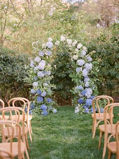 an outdoor ceremony set up with wooden chairs and blue hydrangeas on the grass