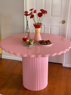 a pink table with flowers in vases on top and pastries on the bottom