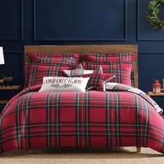 a red plaid comforter set with pillows and pillow cases on the bed in front of a blue wall