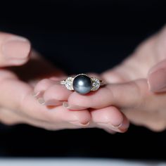 a close up of a person holding a ring with a black pearl in it's middle