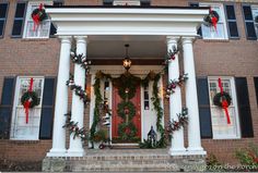 the front porch is decorated for christmas with wreaths and garland on it's pillars