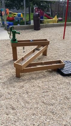 a wooden bench sitting on top of a gravel field next to a playground equipment set