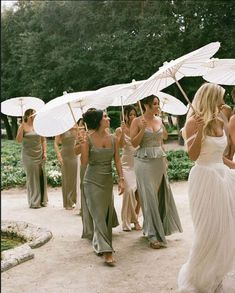 a group of women walking down a road holding umbrellas in their hands and wearing dresses