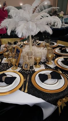 the table is set with black and white plates, gold rimmed place settings, and an ostrich feather centerpiece