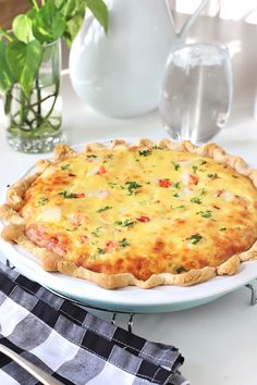 a cheesy quiche on a white plate next to a vase with flowers