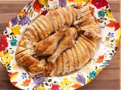 a plate full of sliced chicken on top of a wooden table with colorful flowers and leaves