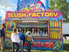 people standing in front of a colorful machine at an amusement park, with the word slush factory written on it