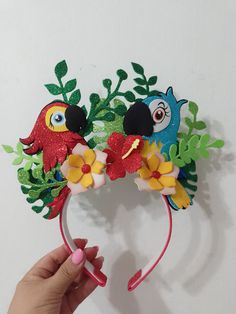 a person holding up a paper headband with two birds on it and flowers in the middle