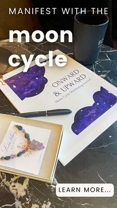 the moon cycle book and pen are sitting on a marble table with a cup of coffee next to it