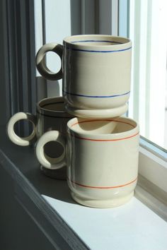 three coffee mugs sitting on a windowsill in front of a window sill