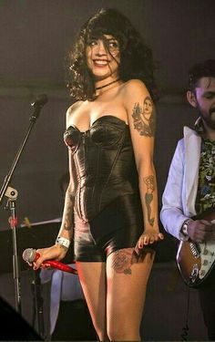 a woman with tattoos on her body standing in front of a microphone and holding a guitar