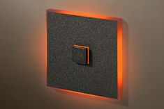 a square light switch on the wall with an orange strip around it's edge