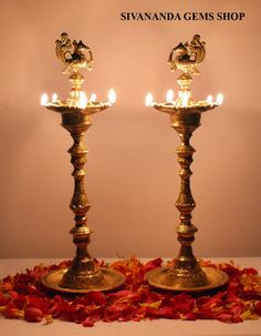 two brass candlesticks with lit candles in them on a white surface surrounded by red flowers