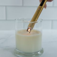 a person holding a toothbrush in a glass of milk with a light on it