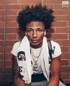 a young man with an afro sitting against a brick wall wearing a white shirt and scarf