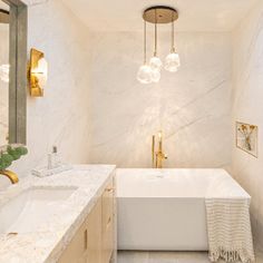 a white bath tub sitting next to a sink under a bathroom mirror and light fixture