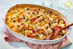 a casserole dish with chicken and vegetables in it next to a glass of water