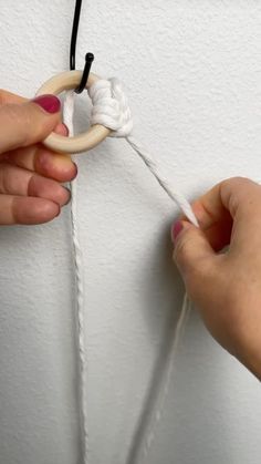 two hands are holding a piece of white yarn and pulling it through the loop with one hand