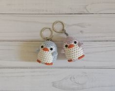 two crocheted keychains are sitting on a white wooden surface, one has an orange beak