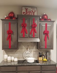 a kitchen decorated for christmas with red bows on the cupboards and decorations above it