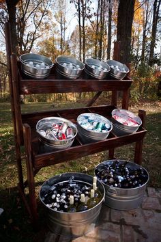 three metal buckets filled with food sitting on top of a wooden shelf next to trees