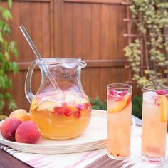 a pitcher and two glasses filled with liquid on a table in front of a fence