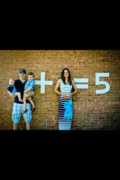 two adults and one child standing in front of a brick wall with the number 5 on it