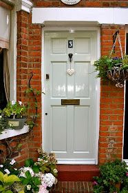 a white front door surrounded by potted plants and hanging baskets on the side of a brick building