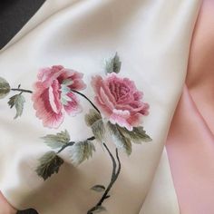 a pink rose on white silk with green leaves and flowers painted on it's side