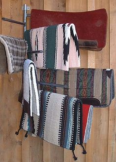 two saddles hanging on a wooden wall with blankets and rugs attached to them