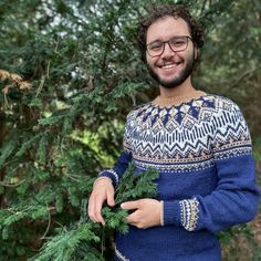 a man in a blue sweater is holding a green plant and smiling at the camera