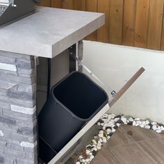 a black trash can sitting next to a stone wall