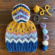 a knitted hat next to yarn and scissors