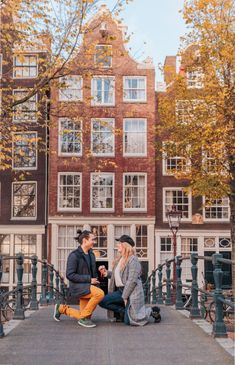 two people sitting on a bench in front of some buildings