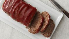 sliced meatloaf with ketchup on a white plate next to a knife