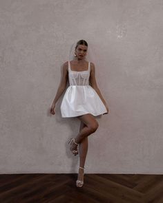 a woman in a short white dress leaning against a wall