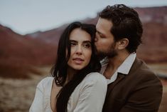 a man and woman standing next to each other in front of the desert mountain range