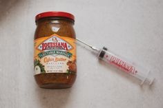 a jar of condiment next to a syringe on a table with food