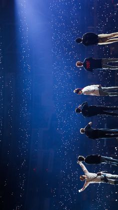 several people standing on stage in front of bright blue lights and raindrops falling from the ceiling