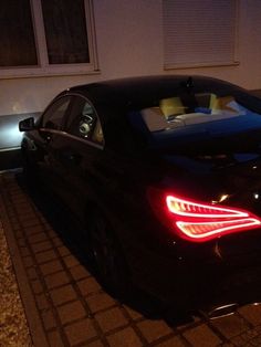 a black car parked in front of a house at night with its trunk lights on