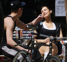 a woman sitting on top of a bike next to a man who is brushing his hair