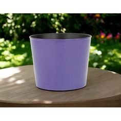 a purple pot sitting on top of a wooden table next to a green bush in the background