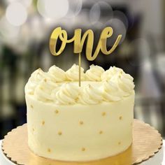 a cake with the word one on it sitting on top of a wooden stand in front of a blurry background