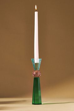 a single white candle sitting on top of a green glass stand with a pink crystal