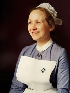 a woman in an apron smiles at the camera while wearing a white hat and blue dress